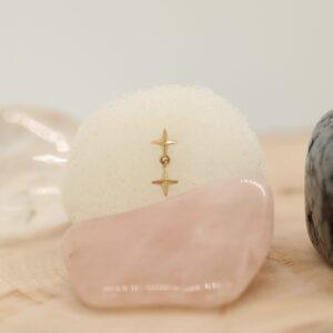 Rozenkwarts en gouden ster-oorbellen op natuurlijke achtergrond.