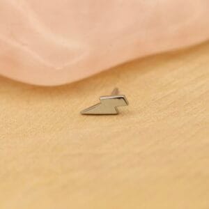 Kleine metalen bliksemsymbool pin op houten oppervlak.